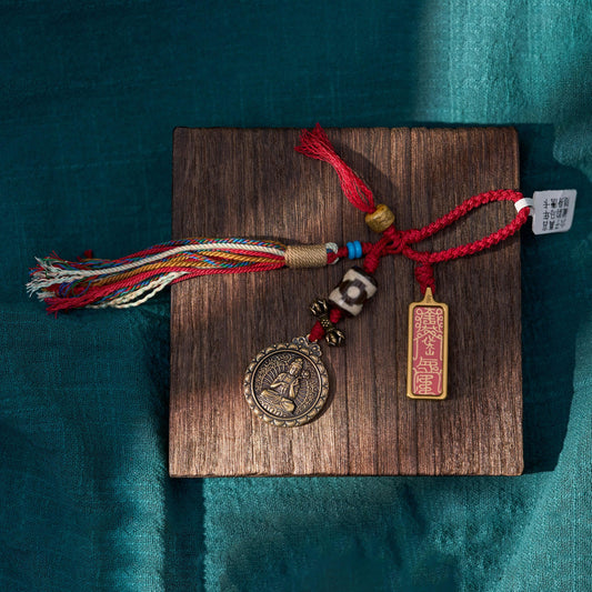 Tibetan-inspired handmade charm with red cord, beads, multicolor tassel, and engraved pendant on wooden board
